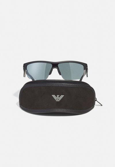 Ochelari de soare negri cu lentile gri, având un design elegant și unghiular. Împreună cu o carcasă neagră cu fermoar, cu detaliu logo pe față.