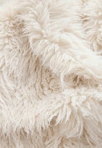 Nærbillede af blødt, off-white fluffy stof med en uldet, tekstureret overflade og lange, krøllede fibre.