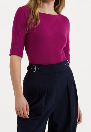 Femme portant un haut magenta ajusté à manches trois-quarts et un pantalon noir taille haute avec ceinture et plis.