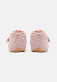 Un par de zapatillas de felpa rosa con suelas de goma, mostradas desde el talón sobre un fondo blanco liso.