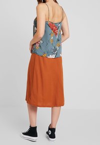 Haut camisole à motif floral en bleu sarcelle, associé à une jupe de couleur rouille, doté de bretelles fines. Porté avec des baskets montantes noires.