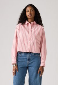 Kuttet rosa skjorte med røde vertikale striper, lange ermer og standard krage, kombinert med høyt liv blå jeans.