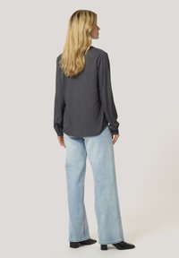 Gray long-sleeve blouse with a relaxed fit, paired with light blue wide-leg jeans and black block-heeled ankle boots.