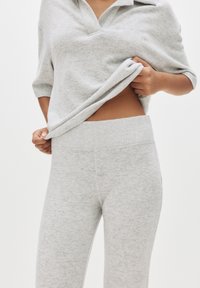 Sivi loungewear set koji se sastoji od kratkih rukava, s kragnom i odgovarajućih visokih hlača, oba izrađena od mekog, teksturiranog materijala.