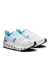 Weiße Sportschuhe mit blauen Akzenten, ausgestattet mit einem strukturierten Mesh-Obermaterial, einer gepolsterten Sohle und markanten Löchern in der Zwischensohle für Flexibilität.