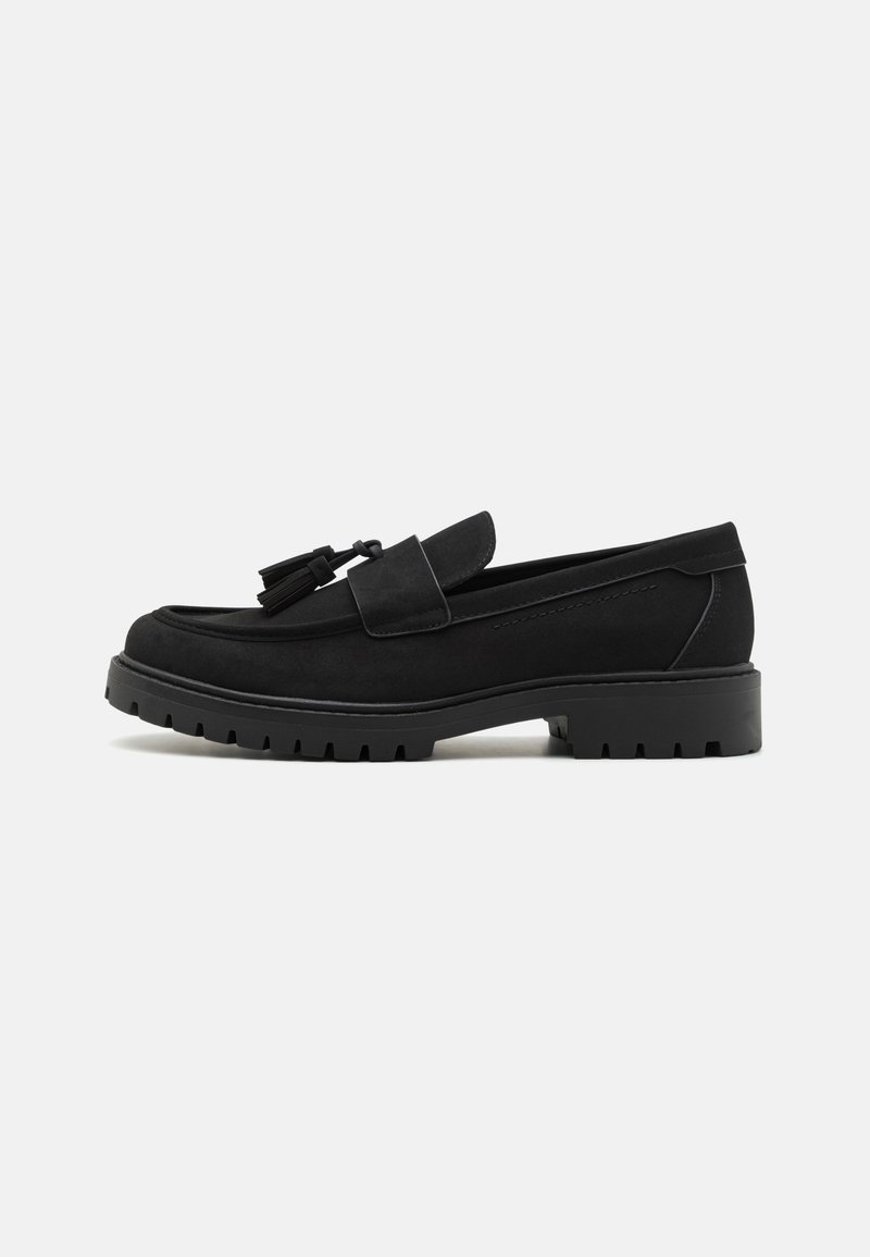 Mocassins de camurça pretos com um bico arredondado, borlas decorativas e uma sola de borracha grossa com um padrão de ranhuras texturizado.