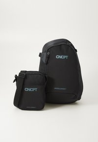 Svart ryggsäck och liten crossbody-väska, båda med blå "CNCP" och "JACK&JONES" logotyper, med en slät och mjuk yta samt blixtlås.