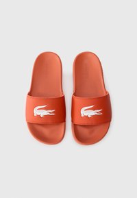 Orange rubber slide sandals featuring a white crocodile logo and textured footbed. Smooth finish with a wide strap design.