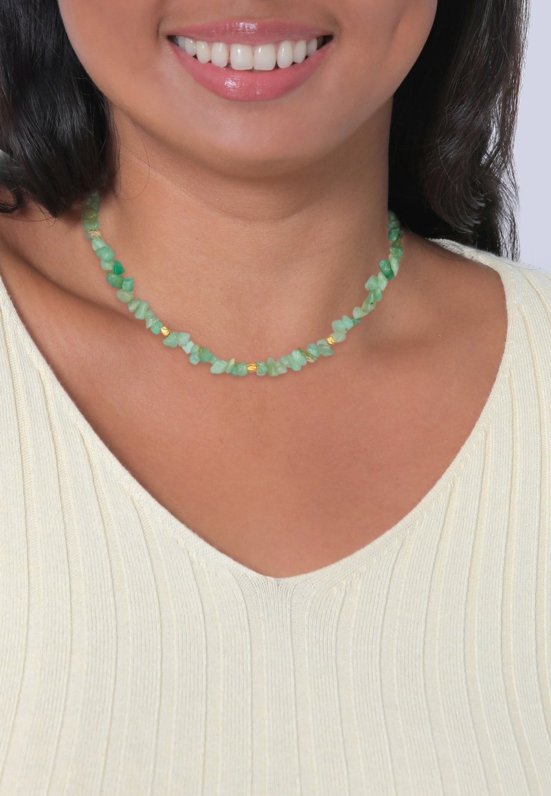 Green gemstone choker necklace with irregularly shaped beads and gold accent pieces, resting against a textured, light-colored shirt.