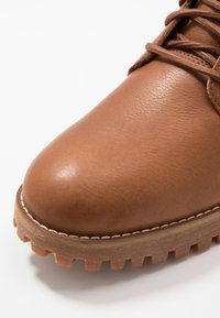 Zapato de cuero marrón con punta redondeada, costuras visibles y parte superior texturizada. Suela de goma gruesa con un patrón irregular para mayor tracción.
