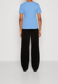 Svetle modré tričko s krátkým rukávem ve spojení s černými manšestrovými širokými kalhotami, které mají strukturovaný povrch a standardní zadní kapsy.