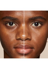 Gros plan d'un visage divisé en deux, mettant en valeur la texture de la peau, des teintes naturelles et un léger éclat sur les lèvres et la peau. Les traits incluent des yeux et des sourcils marron foncé.