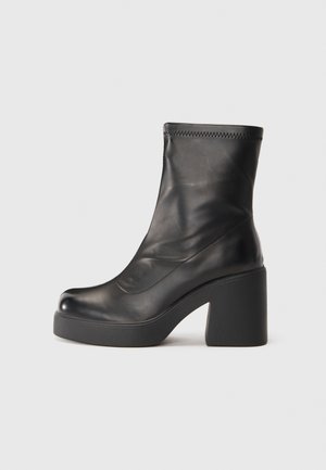 Czarne skórzane botki z gładką fakturą, zaokrąglonym noskiem i masywnym, kwadratowym obcasem. Charakteryzują się eleganckim designem i przeszyciami.