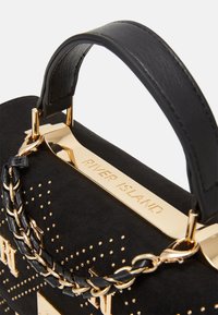 Czarna zamszowa torebka z złotymi ćwiekami, plecionym łańcuszkiem jako uchwytem oraz złotą metalową tabliczką z grawerem "RIVER ISLAND" na górnej krawędzi.