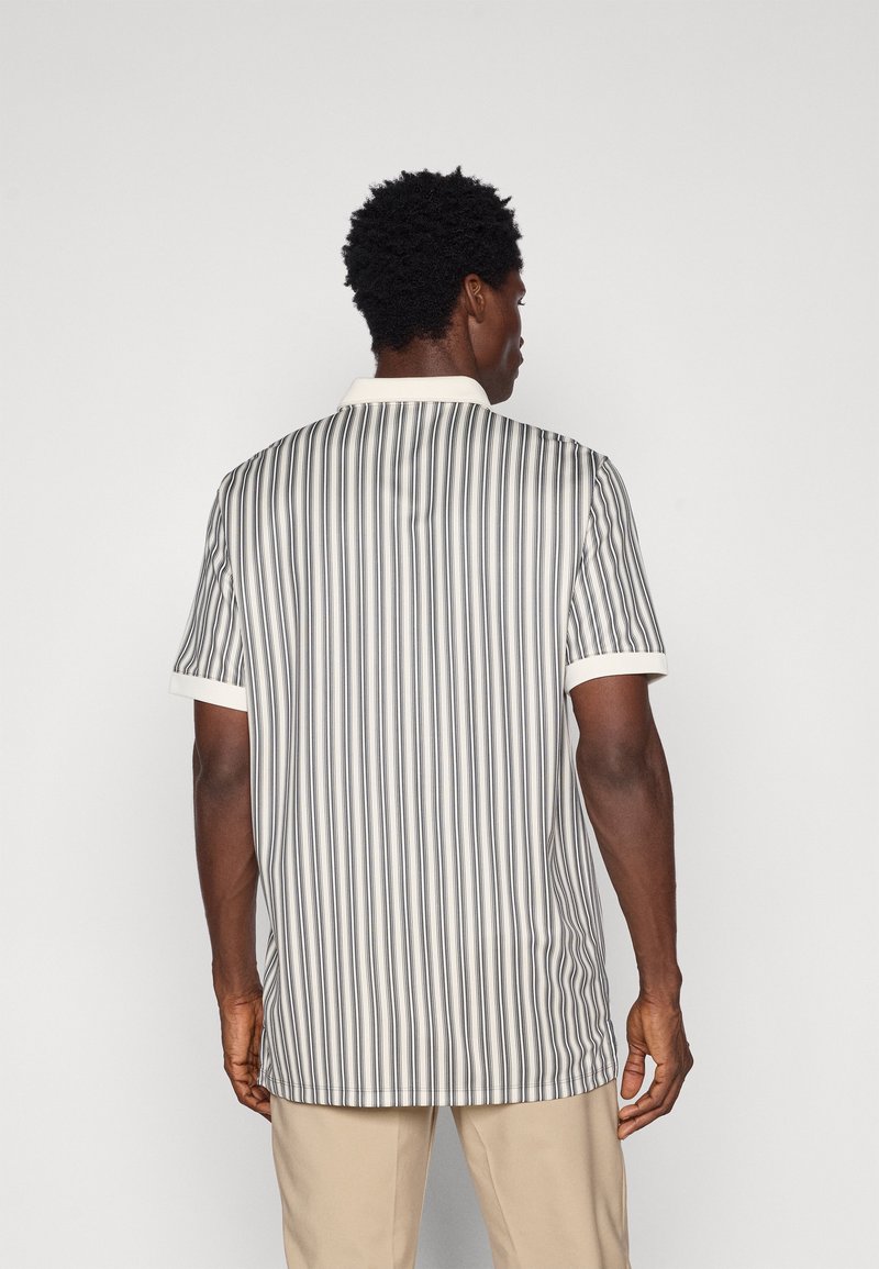 Polo a maniche corte con strisce verticali bianche e nere, colletto chiaro e orlo dritto. Tessuto liscio e leggero.