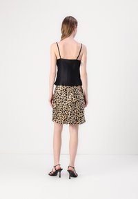 Camisola in satin nero con spalline sottili, abbinata a una gonna con stampa leopardata. Entrambi i capi presentano texture lisce e una silhouette aderente.