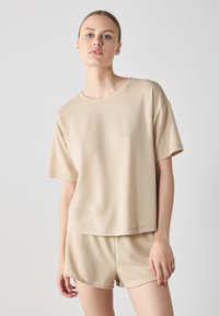 Beige matchande set bestående av en lös sittande t-shirt med kort ärm och shorts. Materialet är mjukt med en slät yta och minimala sömdetaljer.