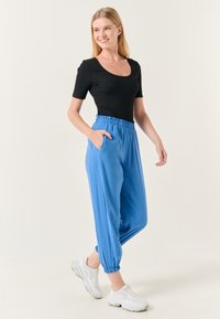 Zwart top met korte mouwen gecombineerd met lichtblauwe, loszittende broek met een elastische tailleband en zijzakken, gedragen met witte sneakers.