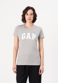 Tricou din bumbac gri, cu mâneci scurte și gât rotund, având un logo mare alb „GAP” imprimat pe față. Design și croi simple.