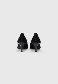 Escarpins noirs en daim avec des bouts pointus et des talons aiguilles fins, présentant une texture lisse et des lignes épurées.