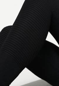 Czarne legginsy z prążkowanym teksturowaniem i gładką dolną częścią, o dopasowanym kroju, który podkreśla ruch i elastyczność.