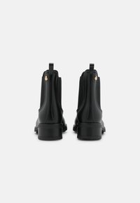 Bottines en cuir noir avec une finition lisse, des panneaux latéraux élastiques et un petit accent doré au niveau du talon. Design à petit talon bloc.