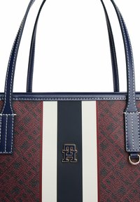 Borsa a mano rossa e navy con motivo testurizzato, caratterizzata da strisce bold in bianco e navy, con un logo dorato e manici robusti.