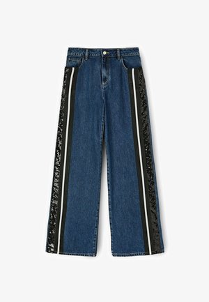 Szerokie dżinsy w ciemnoniebieskim kolorze z czarnymi panelami bocznymi, białymi paskami i akcentami z cekinów. Posiadają tradycyjny pas i zapięcie na guzik.