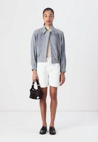 Bomber jacket in suede grigio, dolcevita beige, pantaloni corti bianchi, mocassini neri e una borsa nera testurizzata con un'accenno bianca.