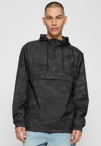 Zwarte camouflage windbreakerjas met een halve ritssluiting aan de voorkant, verstelbare capuchon en elastische boorden, gemaakt van glad, lichtgewicht stof.