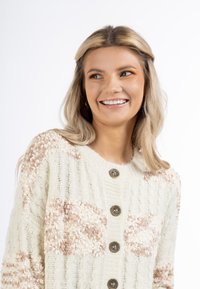 Cardigan crema con accenti texturizzati e fluffy in marrone chiaro. Design a coste, scollo rotondo e cinque bottoni decorativi rotondi.