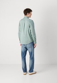 Lys grønn langermet skjorte med knapp-ned krage, bakfolddetalj, kombinert med lyseblå jeans og hvite joggesko.