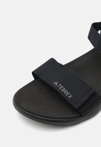 Black sandal featuring a wide fabric strap labeled "TERREX," a textured footbed, and a durable rubber outsole. Designed for comfort and stability.
