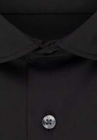 Schwarzer Hemdkragen mit einem dunklen, durch die Knopfleiste befestigten Knopf, Nahaufnahme des oberen Brustbereichs.