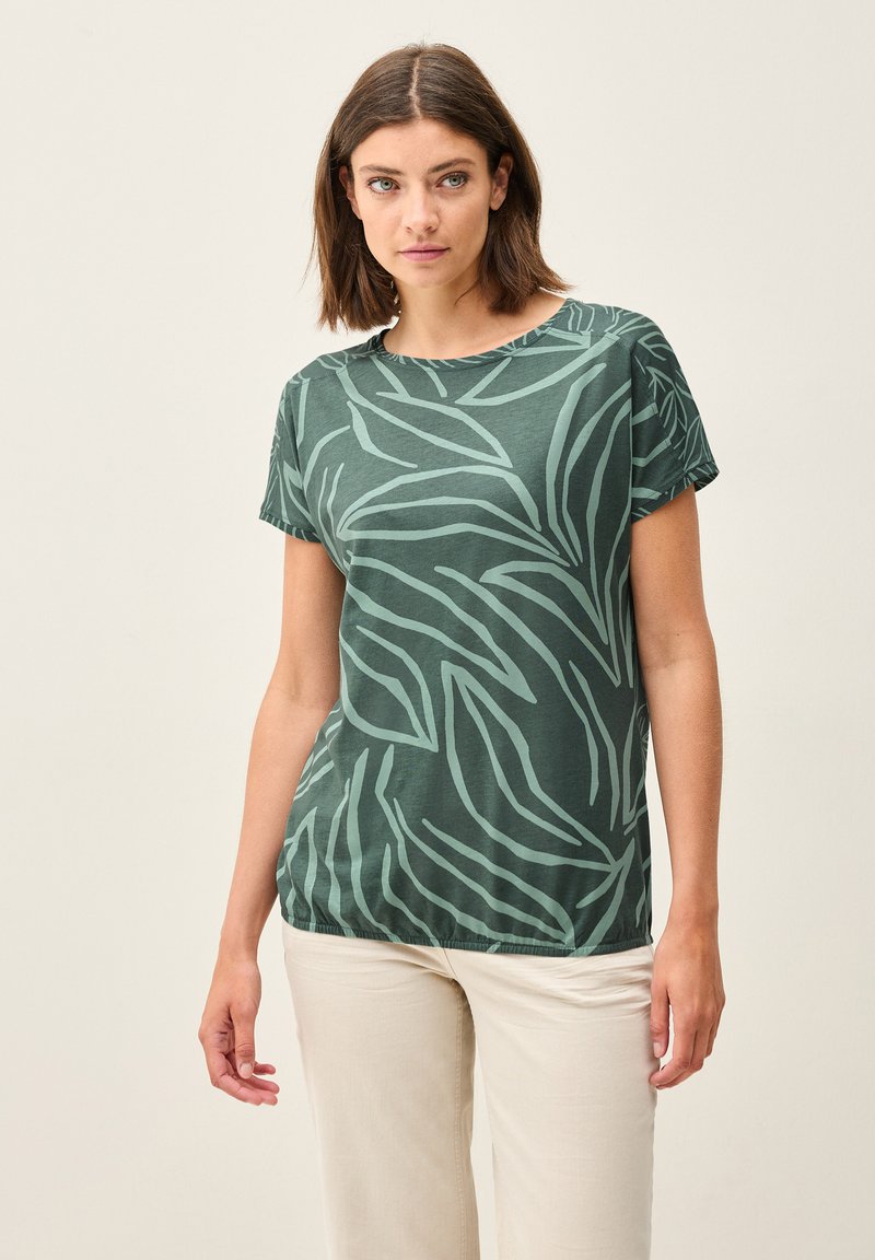 Camiseta verde de manga corta con un patrón de hojas en un tono más claro. Tejido suave, corte relajado, cuello redondo y ligeramente fruncida en el dobladillo.