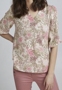 Blumenbluse in Creme mit rosa und grünen Mustern, mit V-Ausschnitt und kurzen Puffärmeln. Glatter Stoff mit leichter Textur.