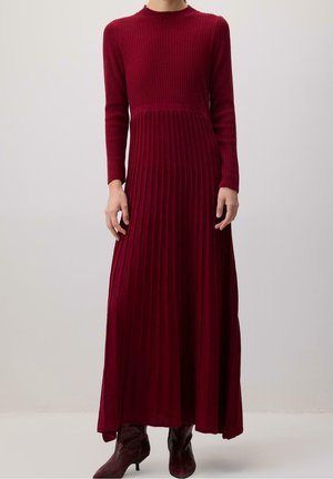 Robe bordeaux côtelée à manches longues avec un corsage ajusté et une jupe évasée, portée avec des bottines à talons bordeaux assorties.