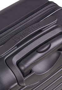 Černý tvrdý kufr s texturovaným povrchem, výsuvnou rukojetí a zipovým uzavřením s vyraženým logem 'American Tourister'.