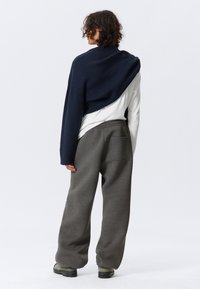 Navyfarbener, gekürzter Pullover, der über einem weißen Langarmshirt drapiert ist, kombiniert mit grauen Sweatpants. Verfügt über eine Gesäßtasche und strukturierter Stoff.