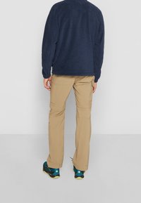 Maglietta a maniche lunghe in pile navy abbinata a pantaloni cargo convertibili beige e scarpe da trekking con dettagli in teal, mostrata da dietro.