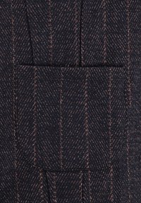 Ciemnoniebieska tkanina w wzór jodełki w jaśniejszych odcieniach. Posiada jedną kieszeń i strukturalną powierzchnię. Dopasowany fason z widocznymi szwami.