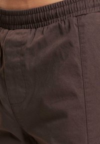 Pantalones con cinturilla elástica marrón, confeccionados con una tela suave y texturizada. Cuentan con bolsillos laterales y un corte relajado, que enfatiza la comodidad y la funcionalidad.