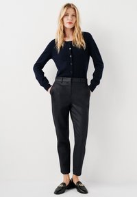 Marinblå cardigan med knappar, kombinerad med svarta skräddarsydda byxor. Slät textur, slim fit, klassisk design. Svarta loafers med kedjedetalj.