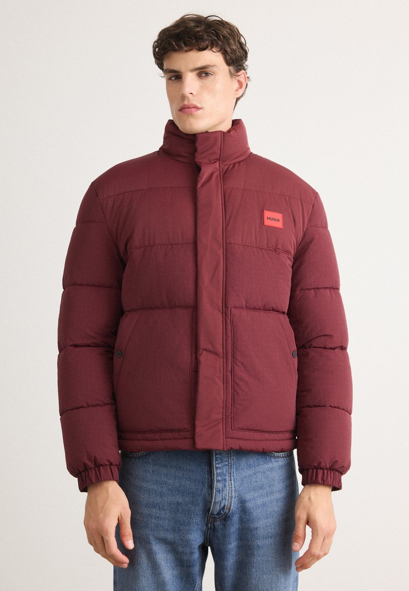 Bordeaux pufferjakke med høj krave, lynlås lukning og logo patch; har quiltet tekstur og elastiske manchetter for en tætsiddende pasform.