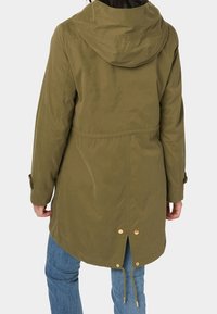 Olivově zelená kapucí opatřená bunda se stažením v pase, elastickým šňůrkem na lemu a kováním ve zlatém tónu. Látka je hladká s matným povrchem.
