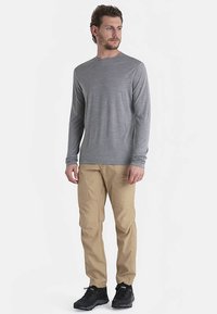 Grijs shirt met lange mouwen en een licht gestructureerd patroon, gecombineerd met beige cargobroek en zwarte sportieve schoenen. Eenvoudig, functioneel ontwerp.