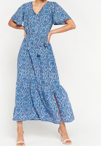 Modrá maxi šaty s výstřihem do V, krátkými rukávy, složitým vzorem paisley a bočním rozparkem. Vyrobeno z lehkého materi álu pro prodyšnost.