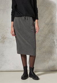 Grauer Midi-Rock aus weichem Stoff mit Kordelzugbund, seitlichen Taschen, kombiniert mit schwarzen Schnürstiefeletten. Glatte Textur, minimalistisches Design.
