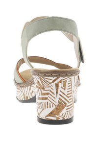Sandales en cuir suédé vert avec un talon en liège et un motif géométrique de feuilles blanches. Bride de cheville ajustable pour un maintien sécurisé.