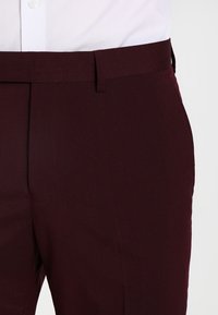 Bordowe spodnie o gładkiej fakturze, slim fit, proste nogawki i płaski przód z klasycznym pasem.